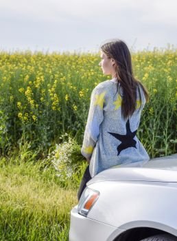 A girl with a bouquet of daisies sits on the hood of the car and looks into the distance.. A girl with a bouquet of daisies sits on the hood of the car and looks into the distance