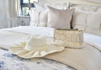 Decorative set with vintage bag and hat on bed in luxury bedroom interior