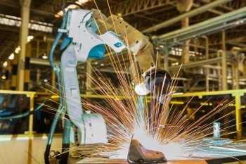 Industrial robot is welding metal part in factory