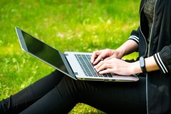 A woman is sitting on the grass while using laptop computer
