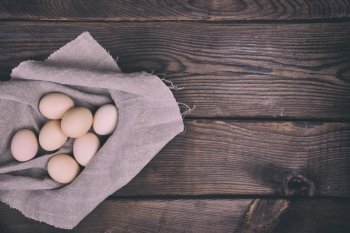 Fresh chicken eggs in shell lie on cloth gray napkin, brown wooden background with free space on the right