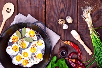 Fried quail eggs in a frying pan on a wooden background, top view