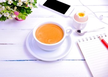 Cup of coffee and notebook with a red pencil on a white wooden background
