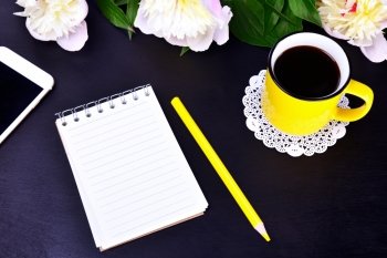 Empty notebook and yellow cup with coffee on black background, top view