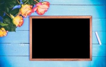 Empty black board and bouquet of yellow roses on a blue wooden background, vintage toning