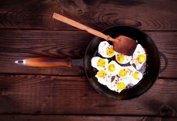 Fried quail eggs in a black frying pan with a wooden handle, top view