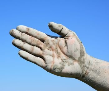 Man’s open palm smeared with mud against the blue sky