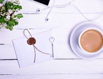 Cup of coffee and a paper sealed envelope on a white table, top view
