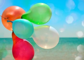 Multicolored balloons flying against the sea in the sun