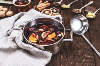 mulled wine in a pan with an iron scoop, behind the ingredients in spoons on a brown wooden background