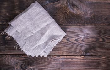 gray linen napkin on a brown wooden background, empty space on the right