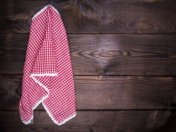 red textile kitchen napkin hanging on a wooden wall, empty space on the right