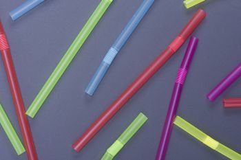 plastic multicolored straws for cocktail are scattered on a black background