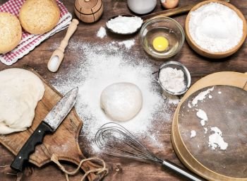 scattered wheat flour on the table, next to raw yeast dough and ingredients for bread making