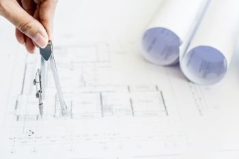 Close-up Of Person’s Hand Drawing Plan On Blue Print with architect equipment
