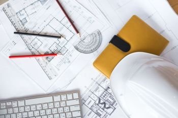 Image of blueprints with level pencil and hard hat on table.