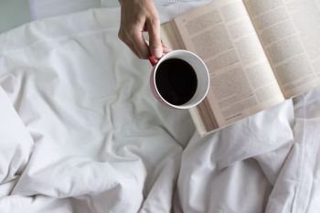 Soft photo of woman on the bed with old book and cup of coffee and copy space.