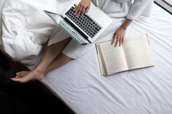 Beautiful young woman in her bed while checking her laptop at home.