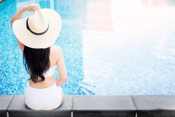 Unrecognizable woman in big hat enjoying relaxing on the swimming pool at luxury villa, travel near the sea and beach in the sunset.