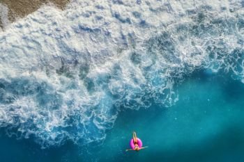 Aerial view of slim woman swimming on the pink swim ring in the transparent turquoise sea in Oludeniz,Turkey. Summer seascape with girl, beautiful waves, blue water in sunny day. Top view from drone
