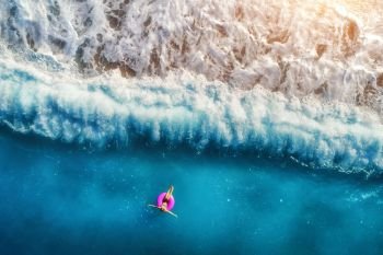 Aerial view of young woman swimming on the pink swim ring in the transparent turquoise sea in Oludeniz. Summer seascape with girl, beach, beautiful waves, blue water at sunset. Top view from drone. Aerial view of young woman swimming in the sea