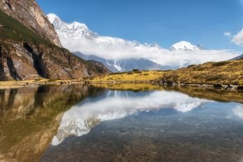Majestic mountains with high rocks with snow covered peaks, mountain lake, beautiful reflection in water, blue sky with clouds in sunset. Nepal. Amazing tranquil landscape with mountains. Himalayas. Majestic mountains with beautiful reflection in water