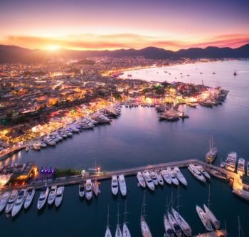 Aerial view of boats and beautiful architecture at sunset. Aerial view of boats and beautiful city at sunset in Marmaris, Turkey. Amazing landscape with boats in marina bay, sea, city lights, mountains, sky, clouds. Top view from drone. Harbor with yacht