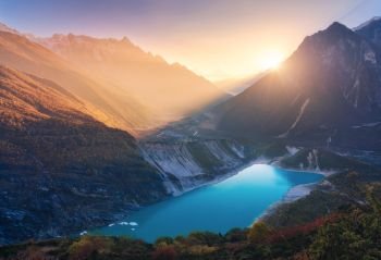 Mountains and lake with blue water at sunset in Nepal. Majestic landscape with high mountains, lake, lightened hills, rocks, yellow sunlight and blue sky. Bright sunny evening. Travel. Nature