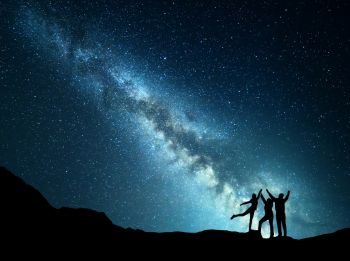 Landscape with colorful green Milky Way. Night starry sky with silhouette of a sporty happy family with raised-up arms on the mountain. Beautiful Universe. Space background