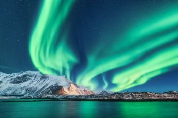 Green northern lights in Lofoten islands, Norway. Aurora borealis. Starry sky with polar lights. Night winter landscape with aurora, sea with sky reflection and snowy mountains. Nature. Travel. Green northern lights in Lofoten islands, Norway. Aurora boreali