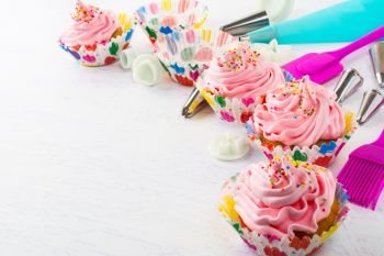 Decorated pink birthday cupcakes  and cookware. Decorated pink birthday cupcakes  and cookware. Birthday homemade cupcakes decorating process. 
Sweet dessert  pastry with whipped cream. 
