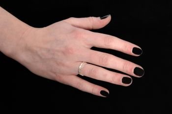 A close up image of the hand of a young woman with her black fingernails and a ring, isolated for black background
