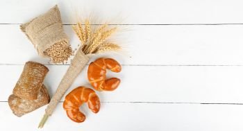 Bread products, ears of wheat, croissants, ciabatta on a white wooden background. Copy space. Top view.