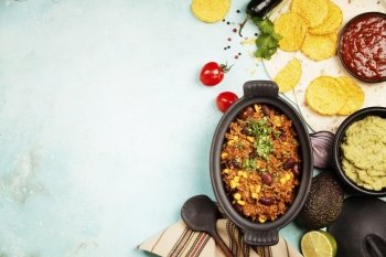 Mexican food concept: tortilla chips, guacamole, salsa, chili with beans and fresh ingredients over vintage background. Top view