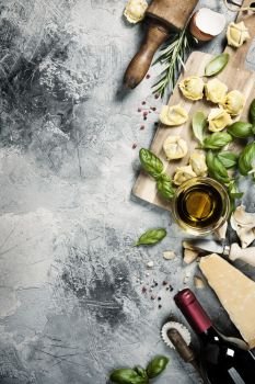 Italian food background with ravioli, vine tomatoes, basil, spaghetti, spinach, onion, parmesan, olive oil, garlic, peppercorns, rosemary and wine. Slate background 