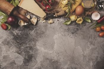 Italian food background with vine tomatoes, basil, spaghetti, spinach, onion, parmesan, olive oil, garlic, peppercorns, rosemary and eggs. Slate background 