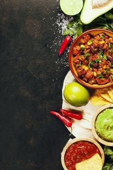 Mexican food concept: tortilla chips, guacamole, salsa, chili with beans and fresh ingredients over vintage rusty metal background. Top view