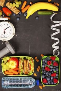 Health & Fitness Food in lunch boxes, measuring tape  and alarm clock on wooden board. Diet food, health and fitness concept
