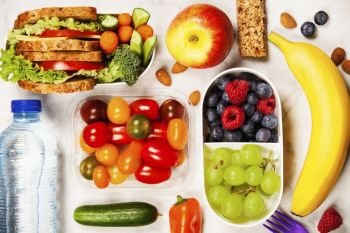 Healthy lunch box with sandwich and fresh vegetables, bottle of water and fruits on wooden background. Top view