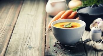 Vegetable cream soup in bowl over old wooden background, copy space