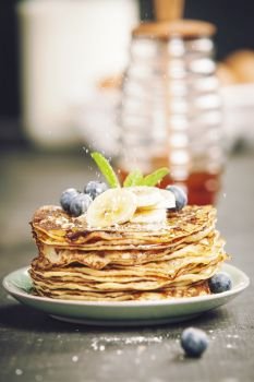 Pancake tower with fresh bananas, blueberries and honey on a rustic table