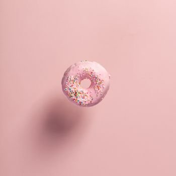 Pink doughnut with sprinkles falling or flying in motion against pink pastel background