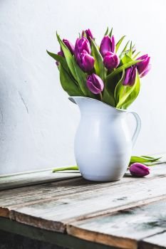 A bouquet of purple tulips in a vase against the wall