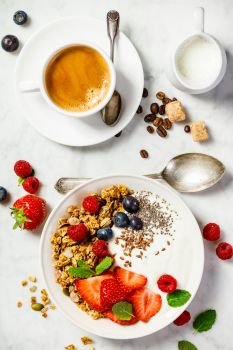 Healthy breakfast with coffee and Bowl of homemade granola with yogurt and fresh berries on white marble background. Top view, flat lay. Healthy breakfast with coffee, yogurt, granola and berries. Healthy breakfast with coffee, yogurt, granola and berries