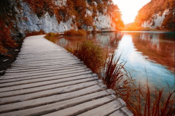 Wooden path across beautiful lake in sunny red autumn forest