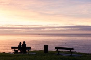 Couple in love on the bench. People silhouette over ocean romantic sunset