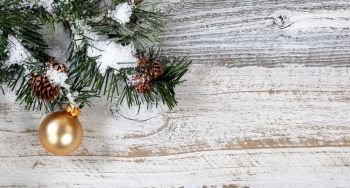 Christmas gold ornament hanging in rough fir tree branch on rustic white wooden background
