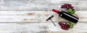 Overhead view of Red wine bottle with grapes, empty drinking glasses and corkscrew on weathered wooden boards