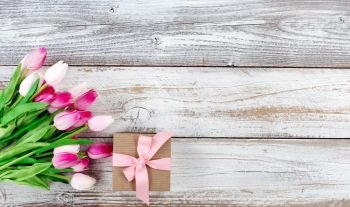 overhead view of a springtime pink tulips and brown gift box on white weathered wooden boards 