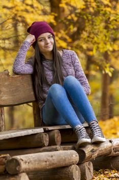 Teenage girl with sneakers seating on bench in autumn park
